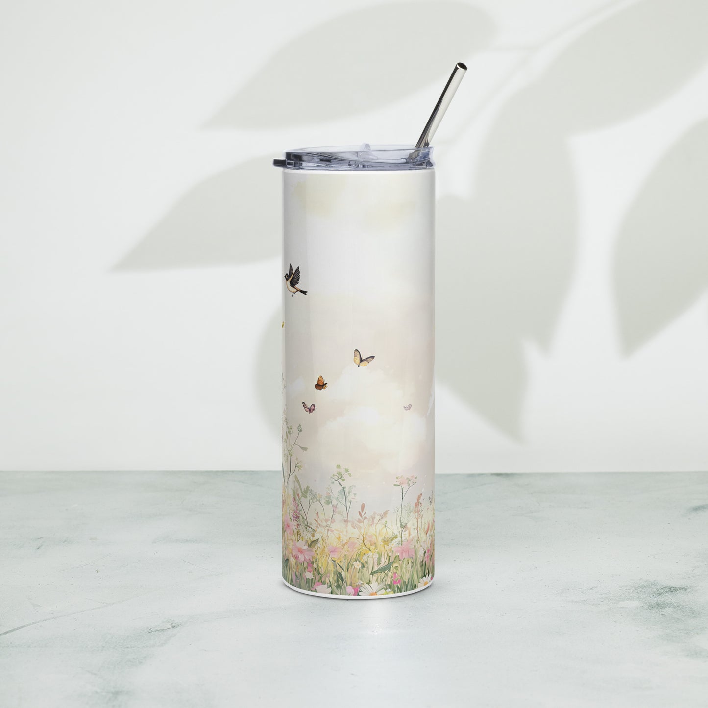 Tall pastel tumbler with floral meadow and butterflies, standing on a light surface with soft plant shadows in the background.
