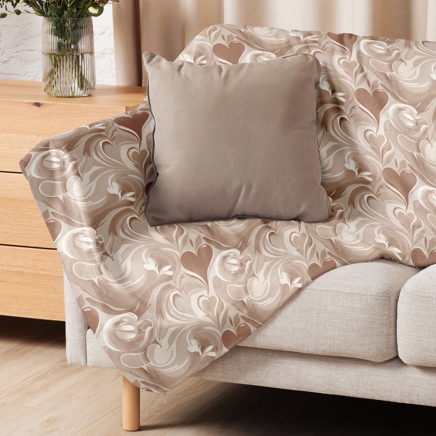 Tan sherpa blanket with swirling cream and brown latte art-inspired pattern, draped over a light beige armchair with a neutral throw pillow, next to a wooden side table and a vase with greenery.