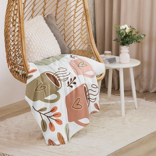 Sherpa blanket in medium size with pastel coffee cup and foliage print draped over a rattan chair – cozy and aesthetic gift for coffee-loving moms.