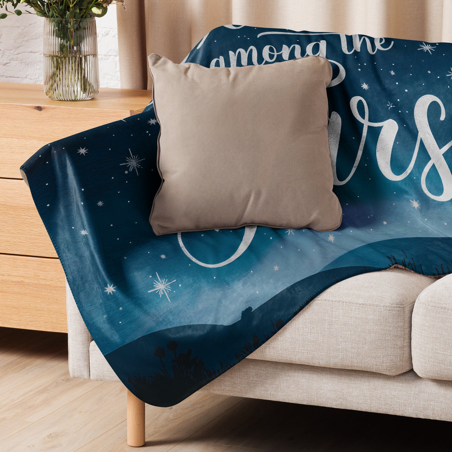 Cozy sherpa blanket with a night sky design draped over a beige sofa, paired with a neutral cushion. Perfect for dreamy evenings and soft home décor.
