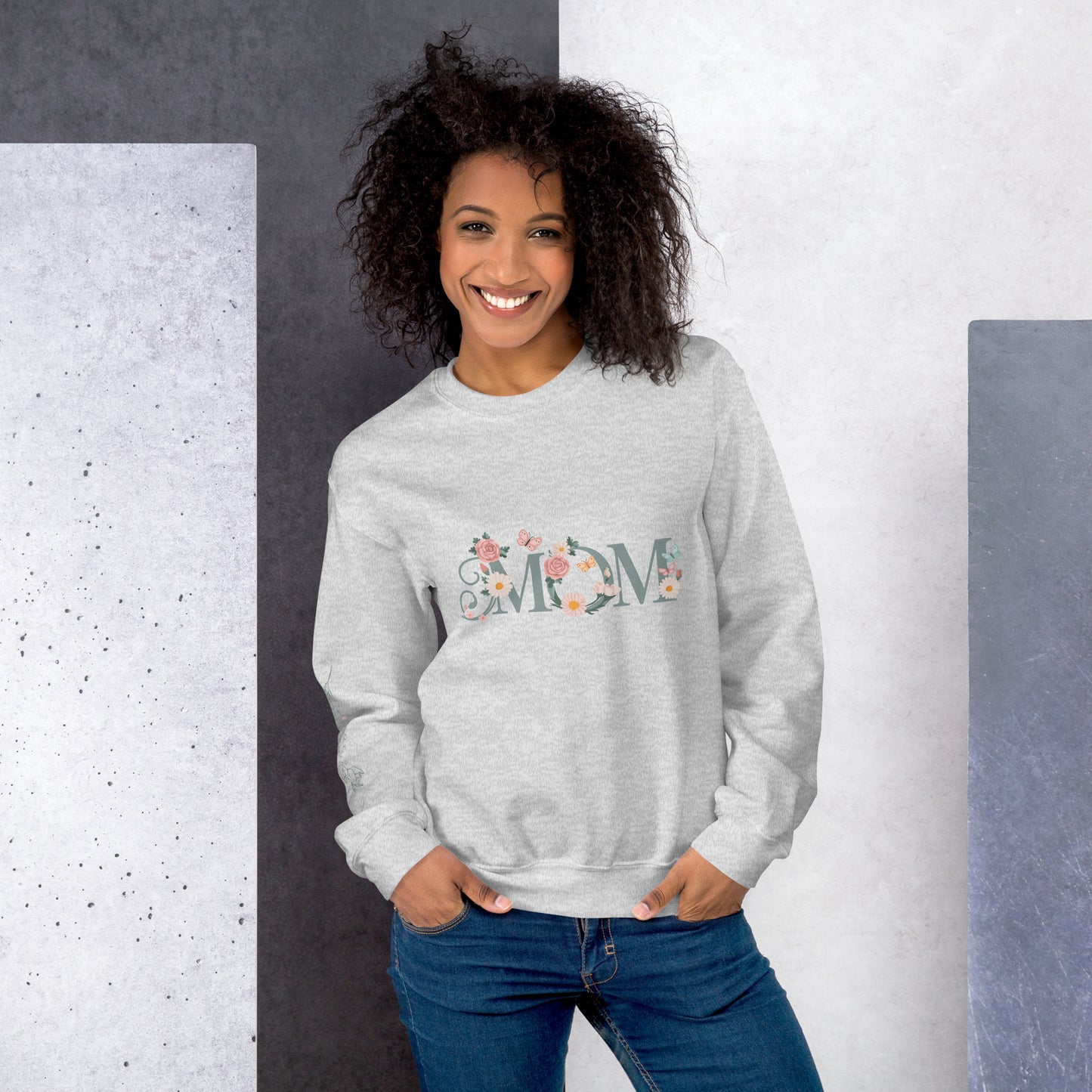 Smiling woman wearing a light grey floral "MOM" sweatshirt, standing against a modern textured background – cozy and stylish gift for moms.