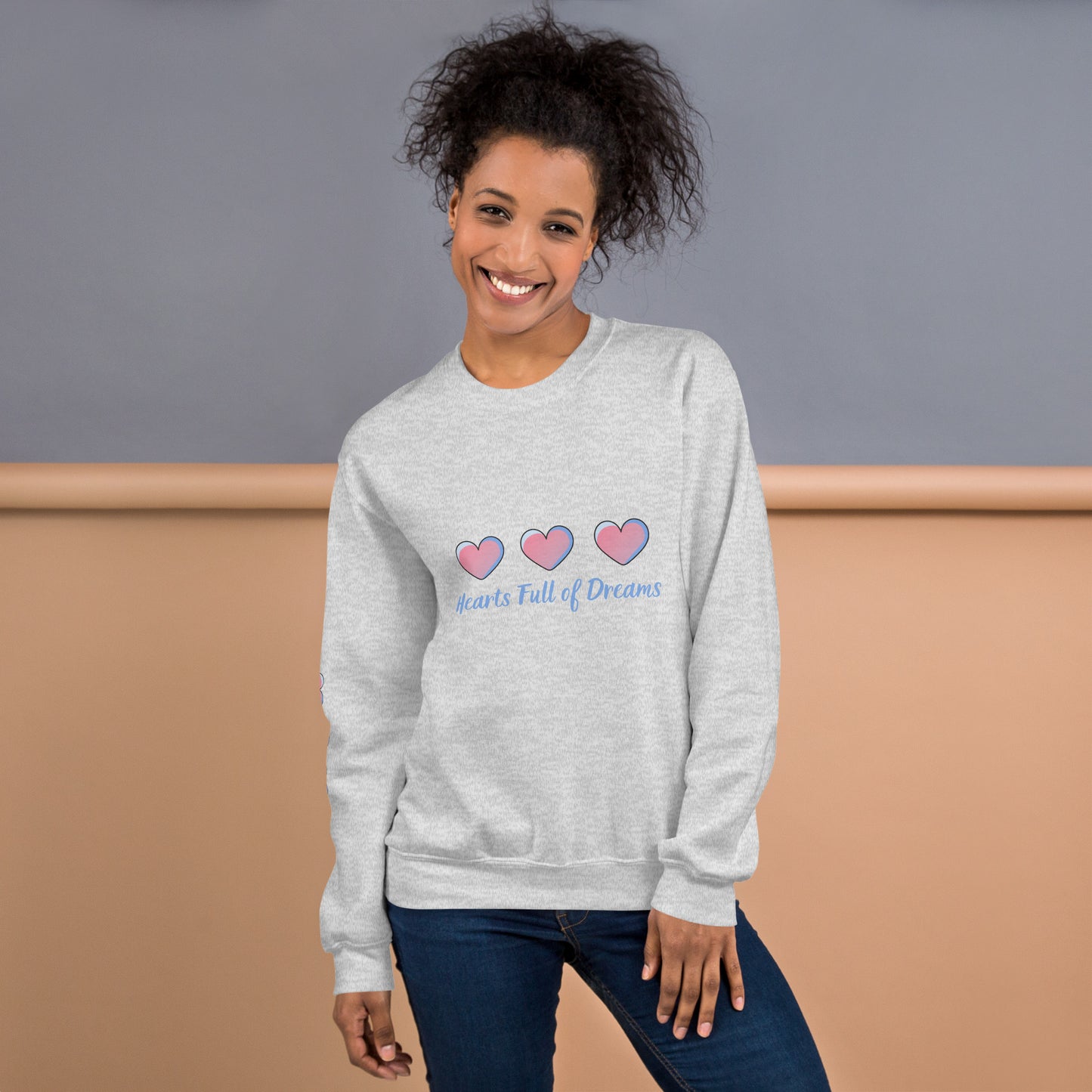 Smiling woman wearing a light gray sweatshirt with a pastel heart design and the phrase “Hearts Full of Dreams”
