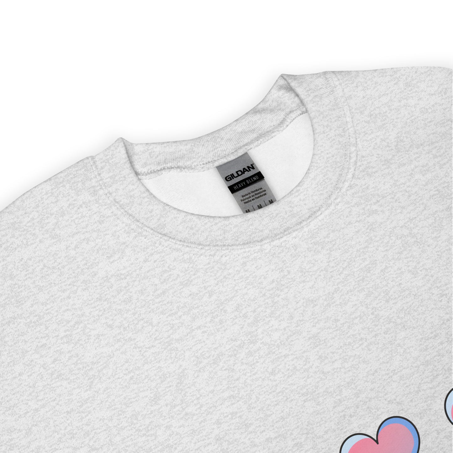 Close-up view of a light gray crewneck sweatshirt with a soft texture, featuring the top part of a pastel heart design near the hem