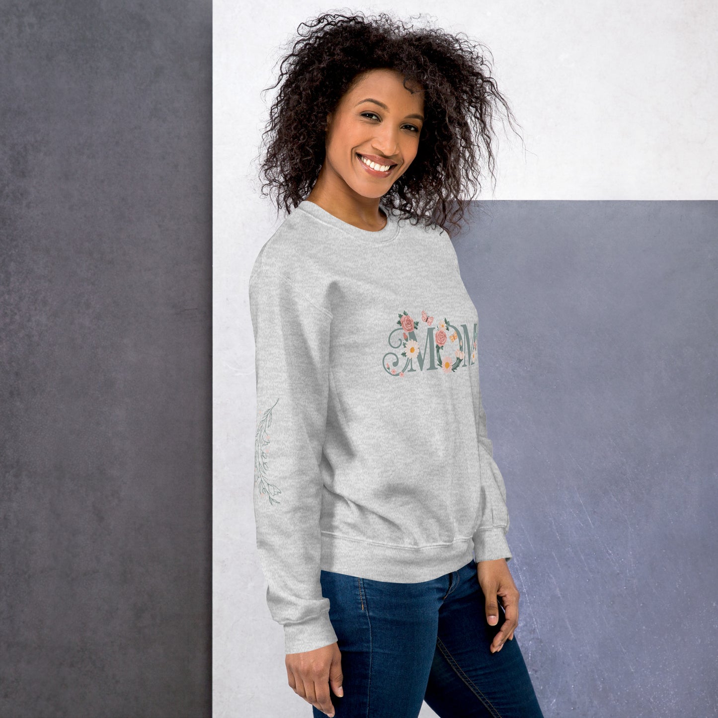 Happy woman wearing a light grey sweatshirt with floral “MOM” text and sleeve detail – cozy and stylish sweatshirt for moms, shown from the right side.