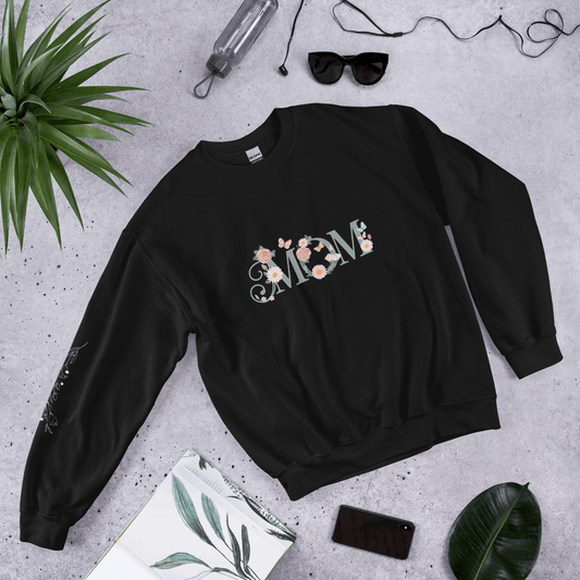 Black sweatshirt with a cute hedgehog and “Born to be wild… but adorable” text, styled flat lay with sunglasses, phone, and green leaves.