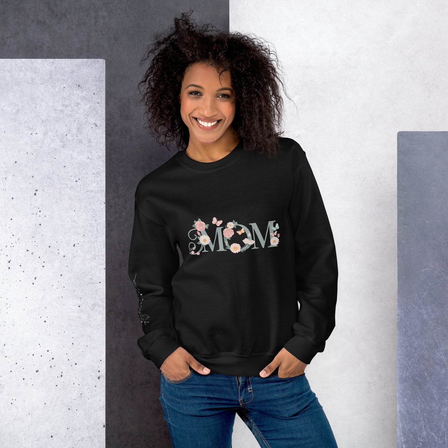Smiling woman wearing a black floral "MOM" sweatshirt, standing against a modern textured background