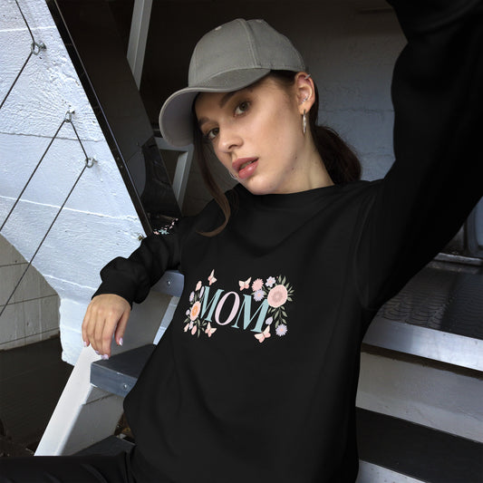 Young woman in a gray baseball cap posing in a cozy black sweatshirt with pastel floral “MOM” design – casual street-style vibe with a soft, feminine twist.
