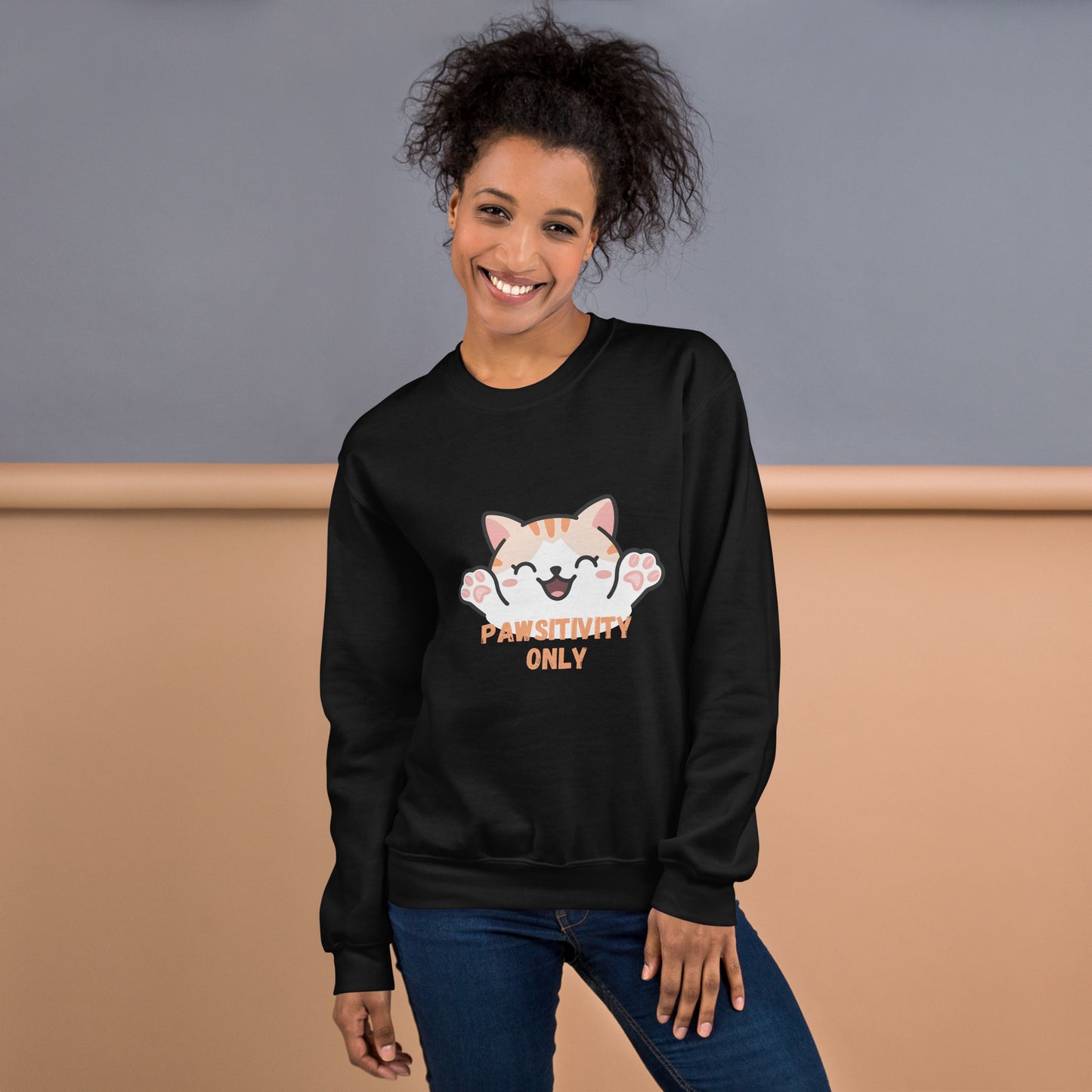 Smiling woman wearing a black sweatshirt with a cute orange cartoon cat and text that says 'Pawsitivity Only' on the front