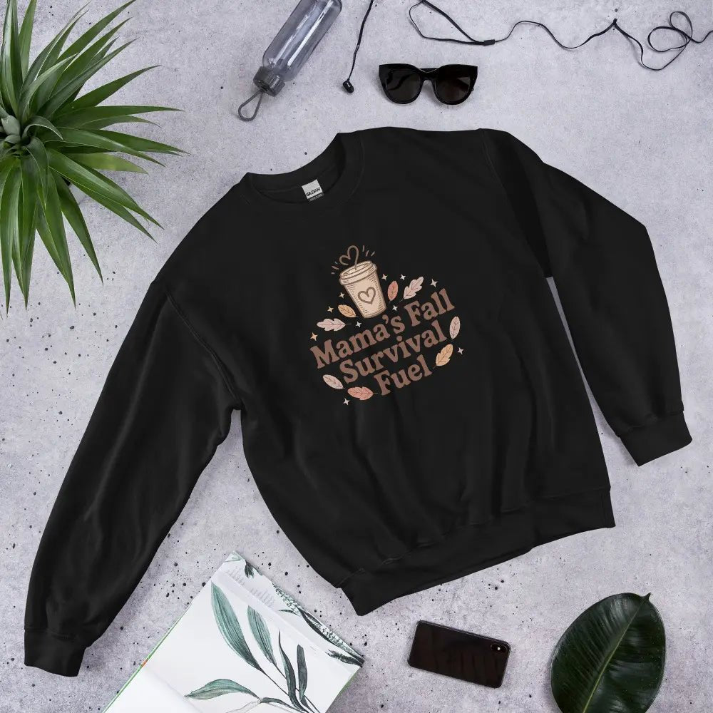 Black sweatshirt with 'Mama's Fall Survival Fuel' text and graphics on a gray surface with accessories.