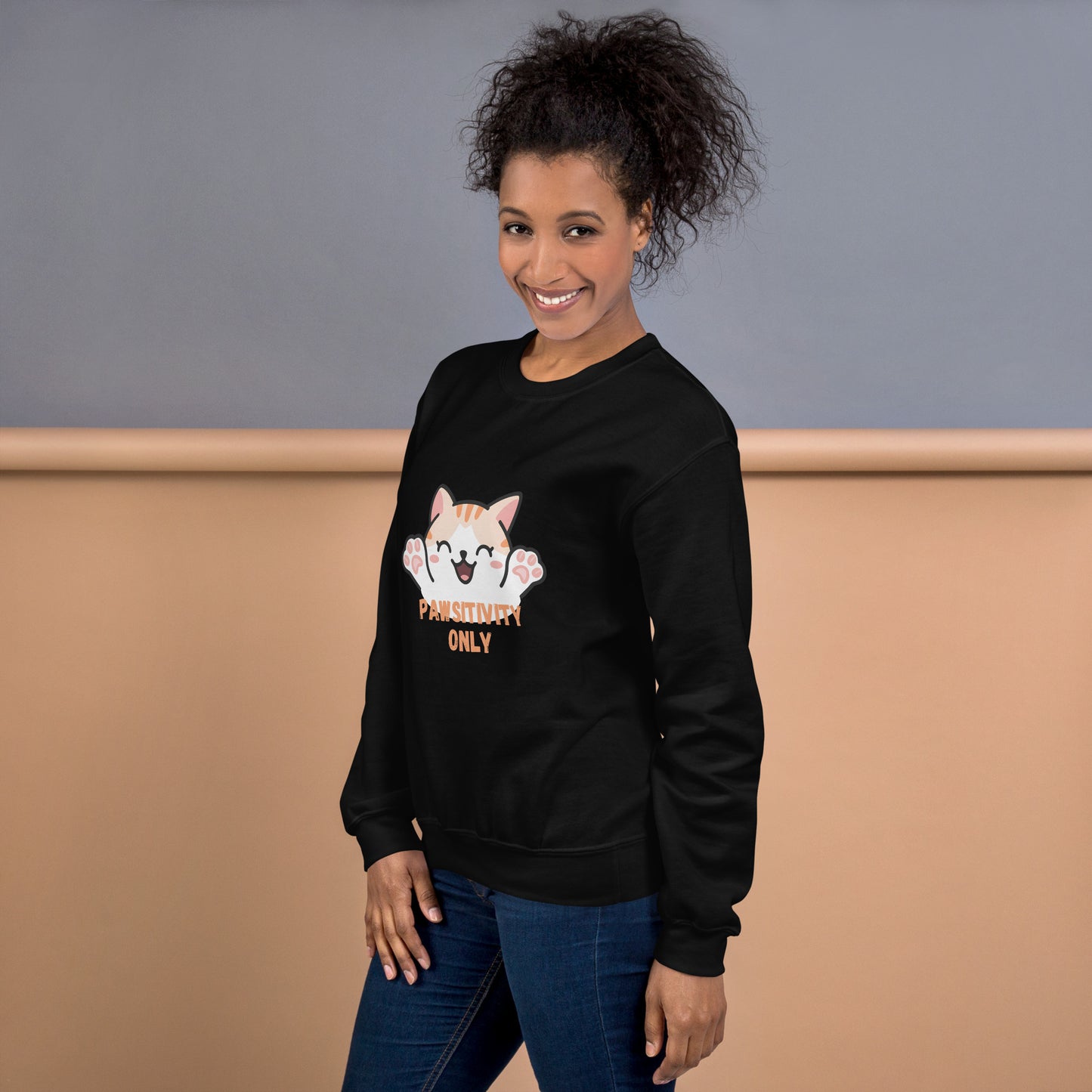Side view of a smiling woman wearing a black crewneck sweatshirt with a cute cat design and text “Pawsitivity Only”