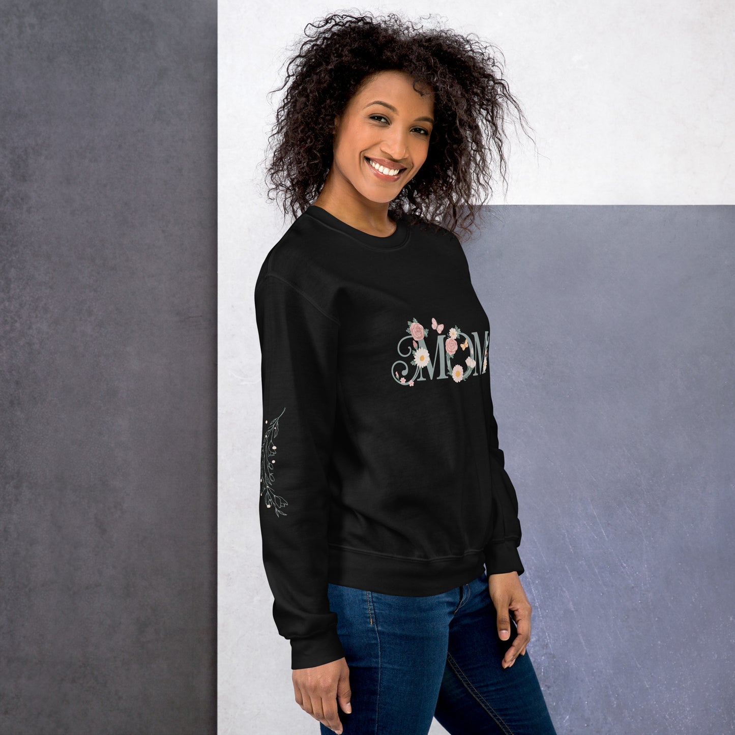 Happy woman wearing a black sweatshirt with floral “MOM” text and sleeve detail – cozy and stylish sweatshirt for moms, shown from the right side.