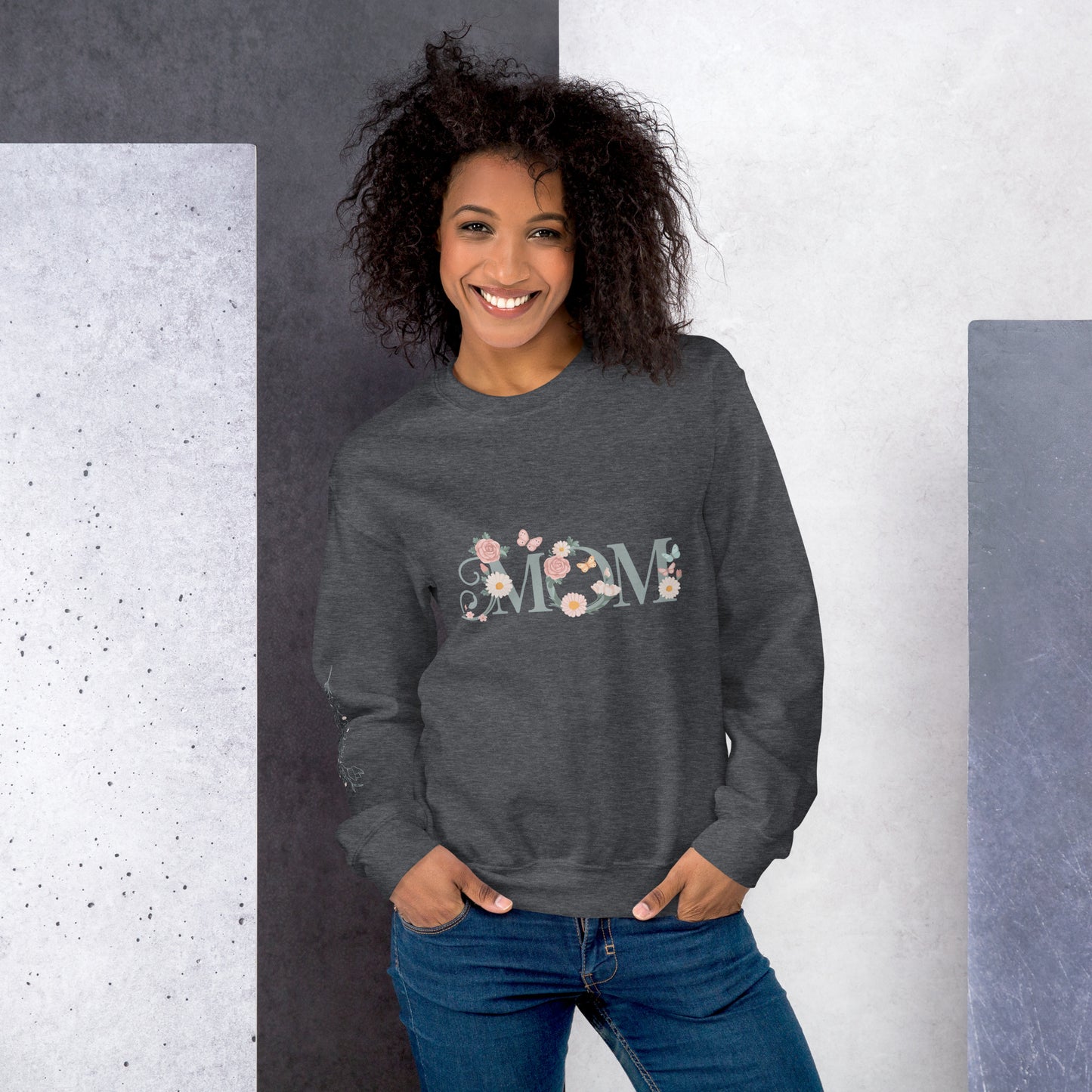 Smiling woman wearing adark heather floral "MOM" sweatshirt, standing against a modern textured background – cozy and stylish gift for moms.
