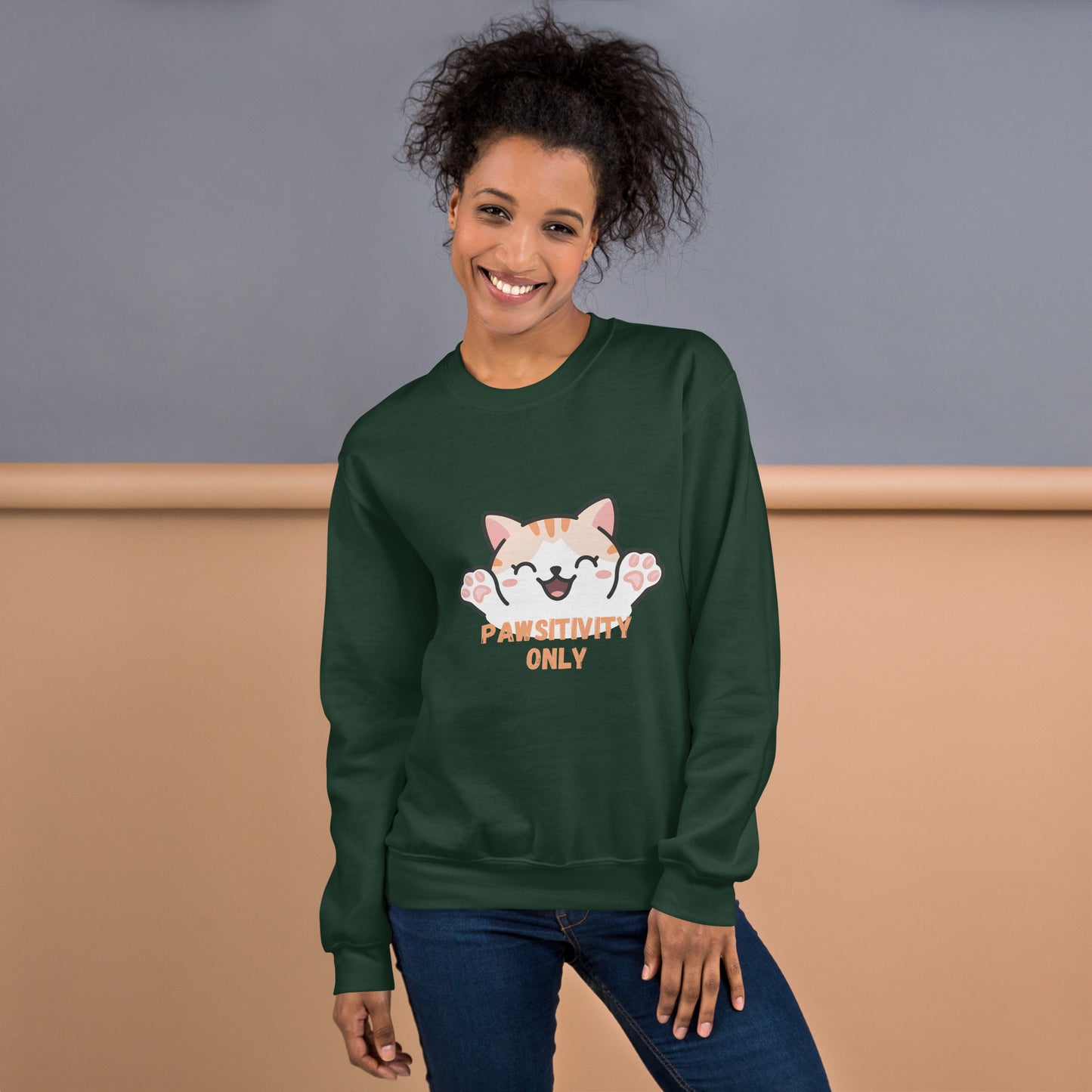 Smiling woman wearing a forest green sweatshirt with a cute orange cartoon cat and text that says 'Pawsitivity Only' on the front