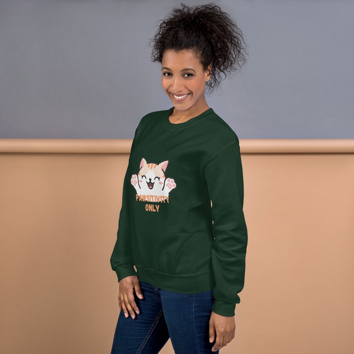 Side view of a smiling woman wearing a forest green crewneck sweatshirt with a cute cat design and text “Pawsitivity Only”