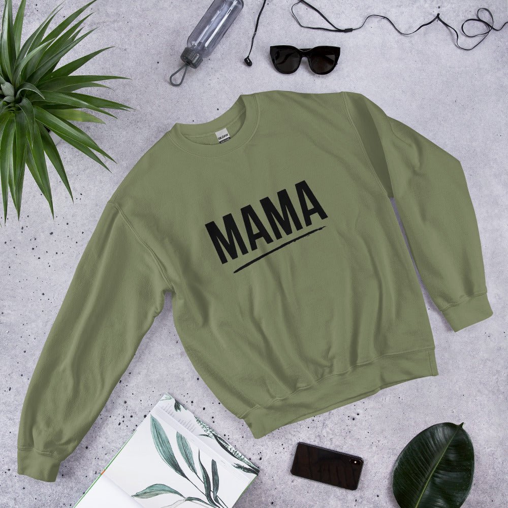 Flat lay of military green MAMA sweatshirt with bold black text and underline, surrounded by sunglasses, a plant leaf, notebook, and smartphone