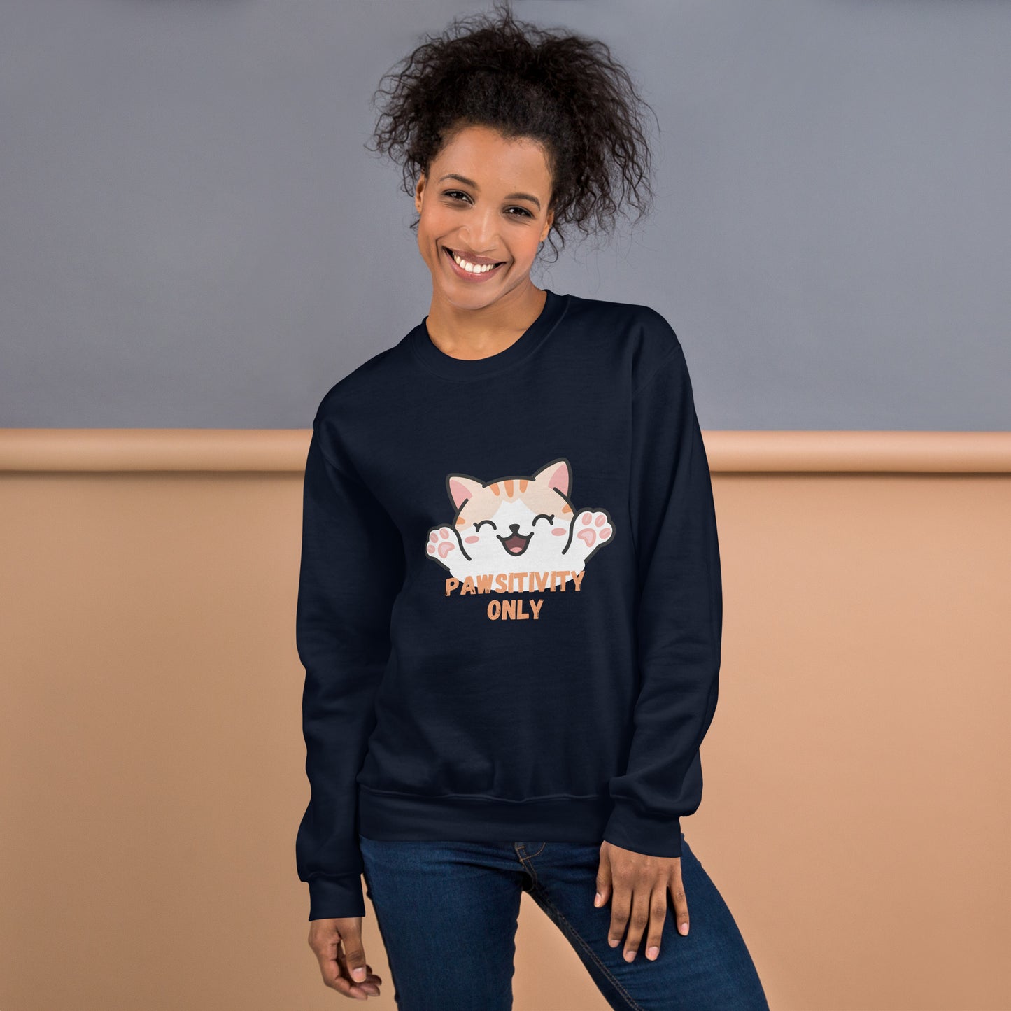 Smiling woman wearing a navy blue sweatshirt with a cute orange cartoon cat and text that says 'Pawsitivity Only' on the front
