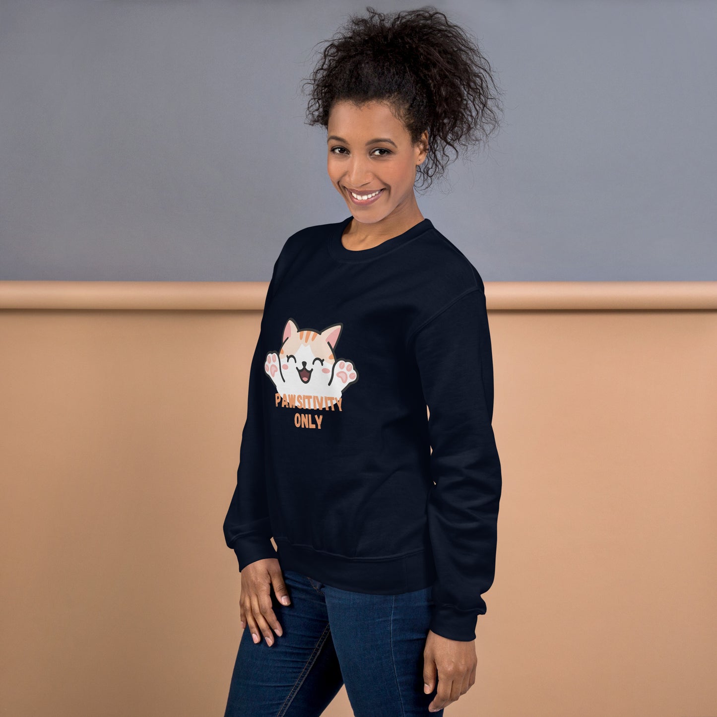Side view of a smiling woman wearing a navy blue crewneck sweatshirt with a cute cat design and text “Pawsitivity Only”