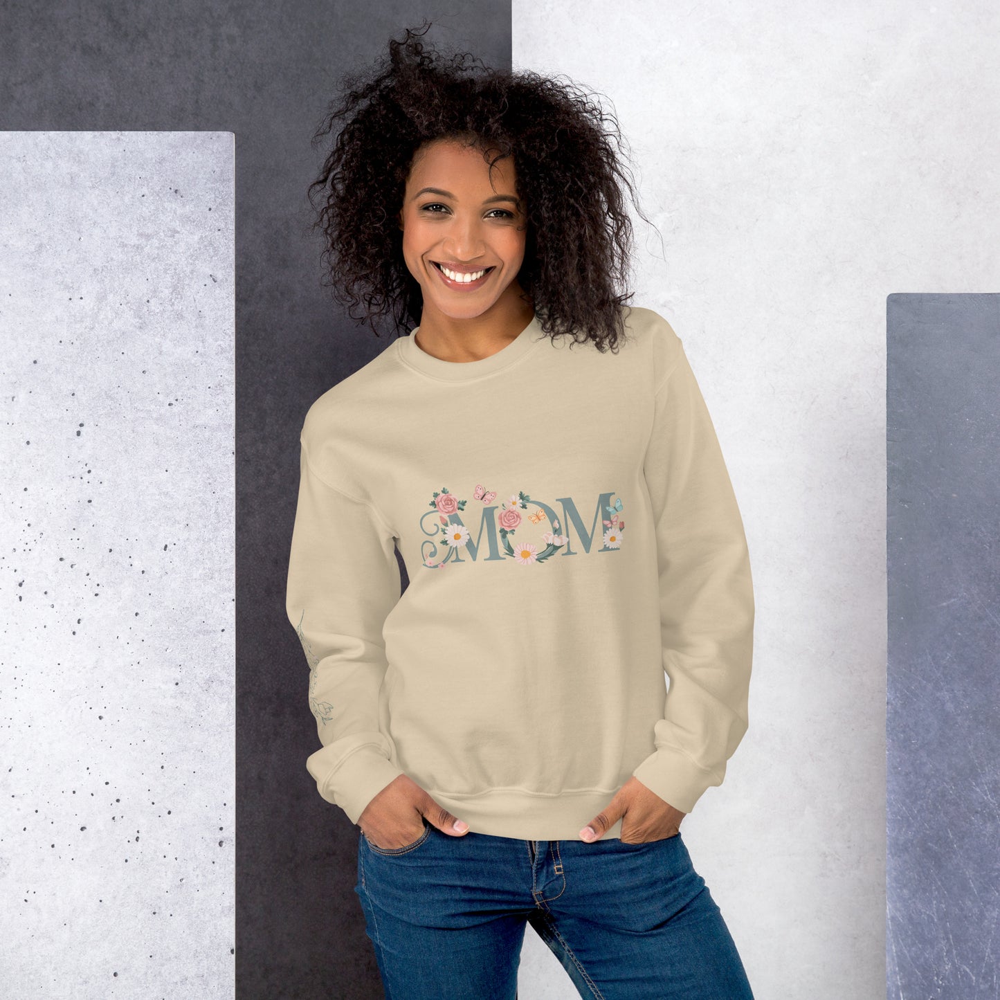 Smiling woman wearing a cream floral "MOM" sweatshirt, standing against a modern textured background – cozy and stylish gift for moms.