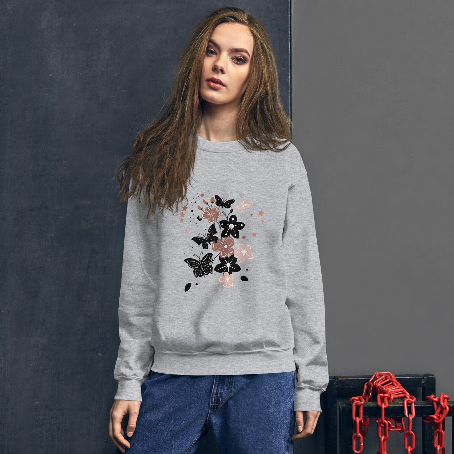 Woman wearing a sport gray sweatshirt with a black and pink floral butterfly design on the chest, standing in front of a dark textured wall.