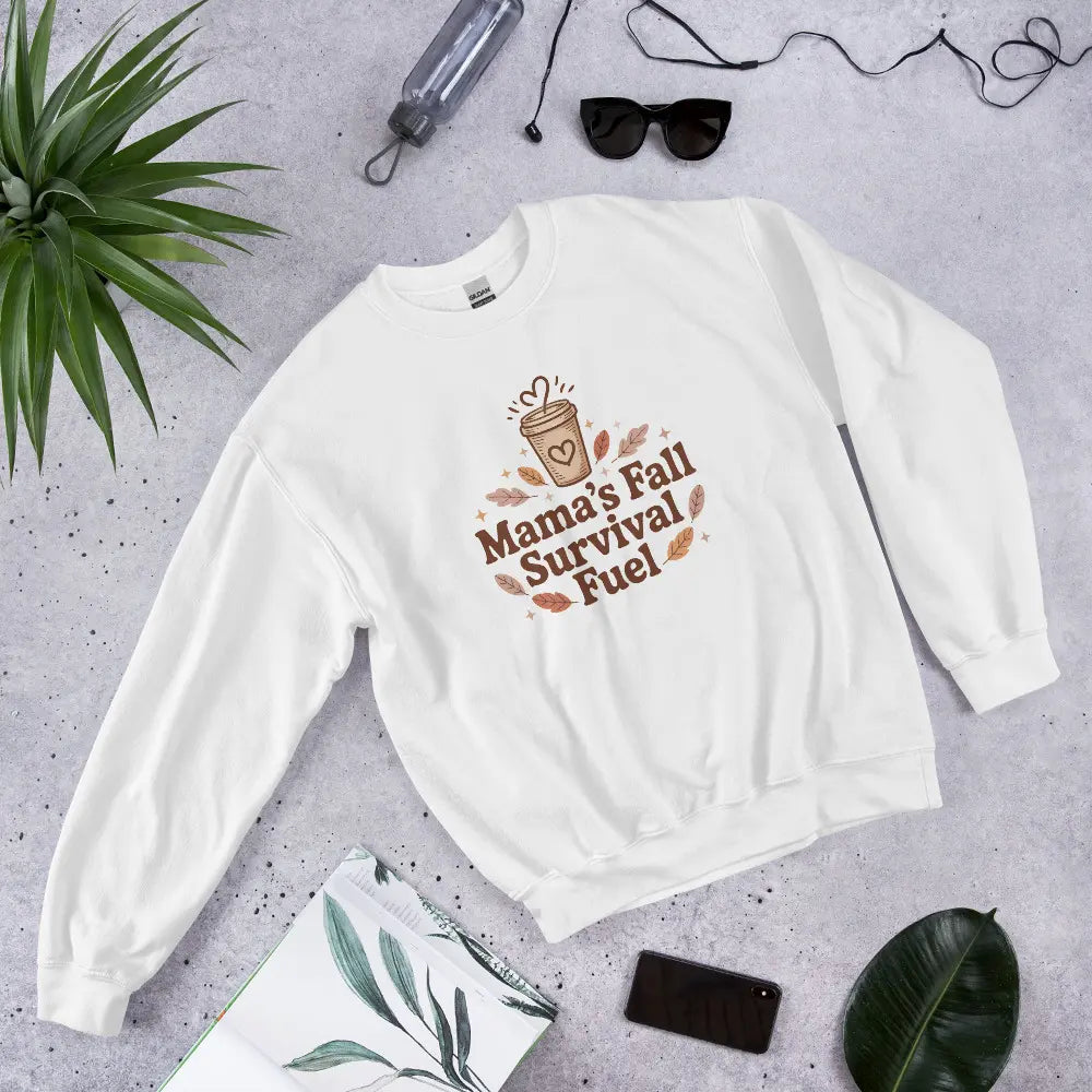 White sweatshirt with 'Mama's Fall Survival Fuel' text on a gray surface with accessories.