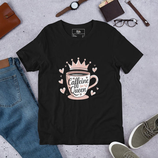 Flat lay of a black unisex t-shirt with a pink “Caffeine Queen” coffee cup design, styled with jeans, sneakers, and accessories.
