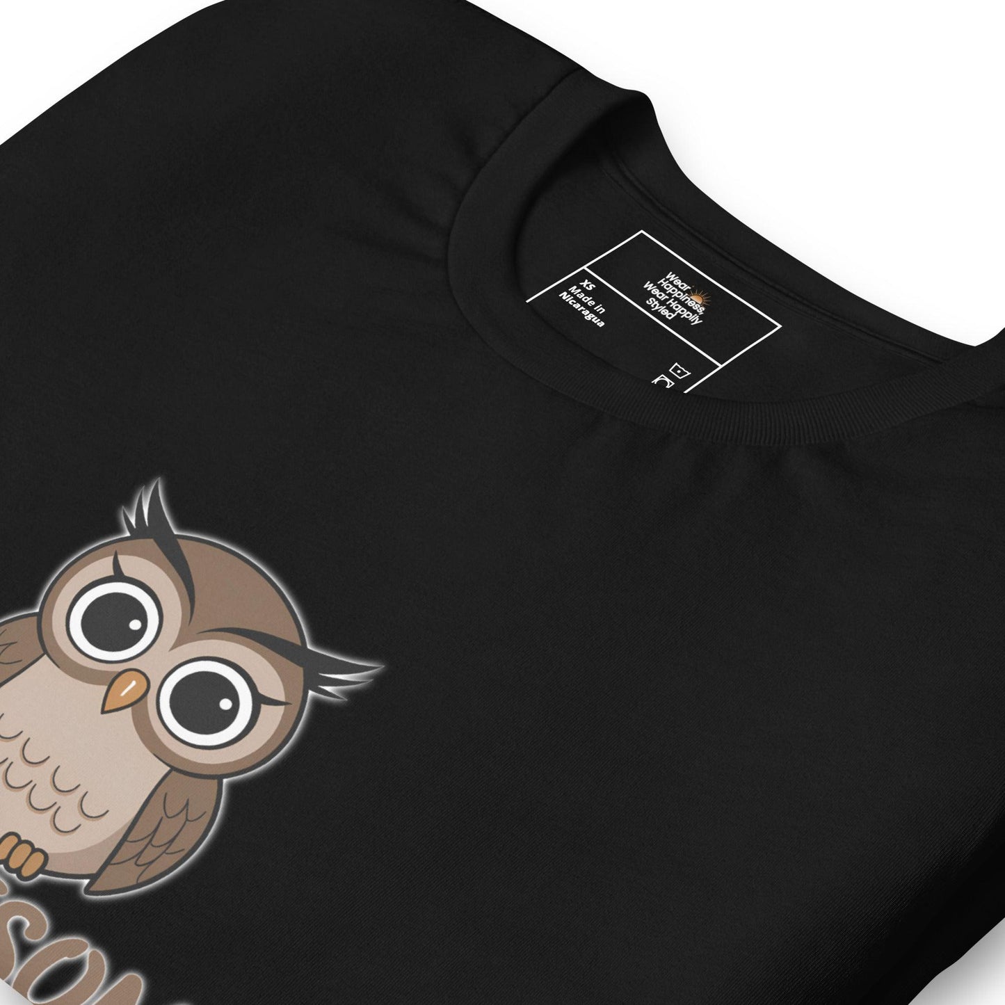 Close-up of a black t-shirt featuring a cute cartoon owl with large, expressive eyes and a "XS" size tag.
