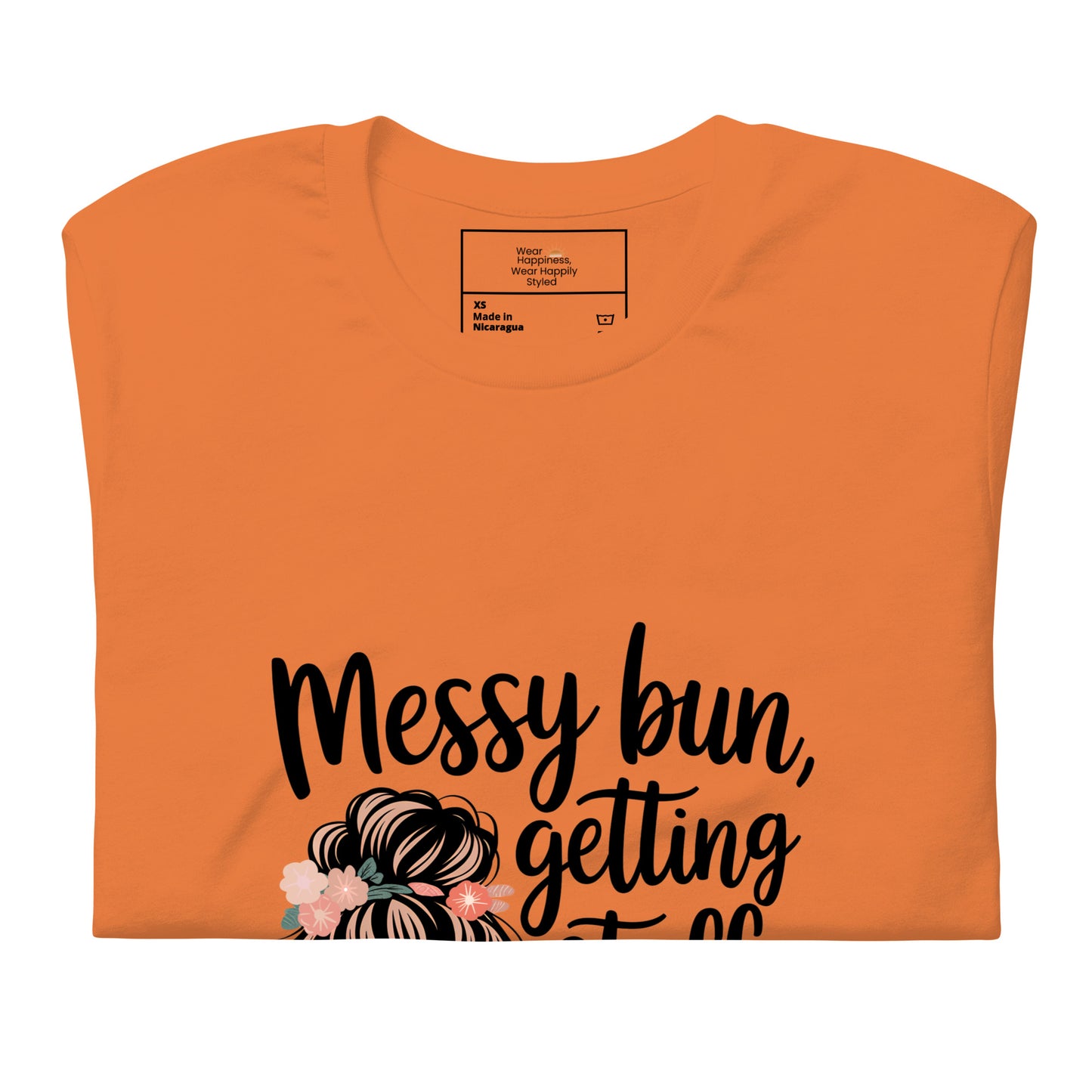 Folded orange t-shirt showing black handwritten text 'Messy bun, getting stuff done' with a messy bun illustration and floral details