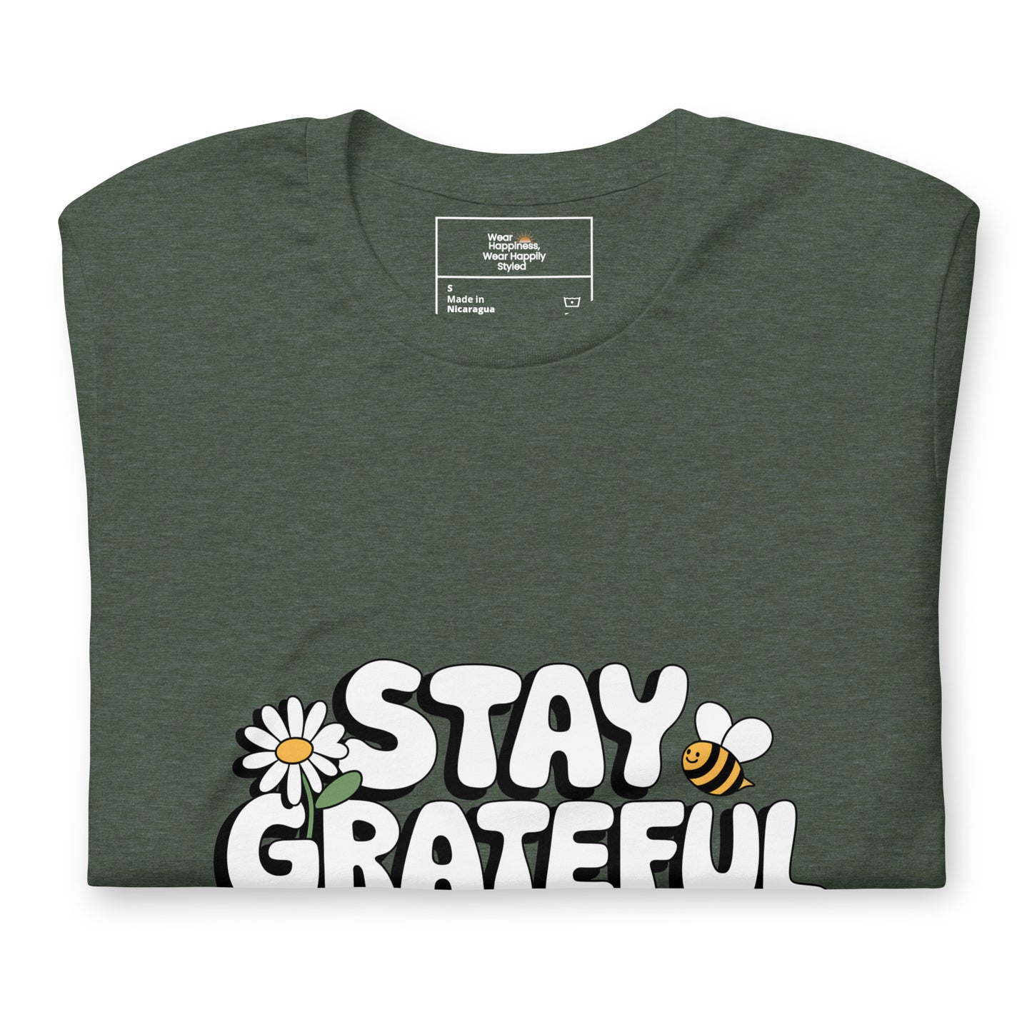Folded forest green t-shirt with a bold white “Stay Grateful” design, featuring a daisy flower and a bee illustration, displayed on a white background.