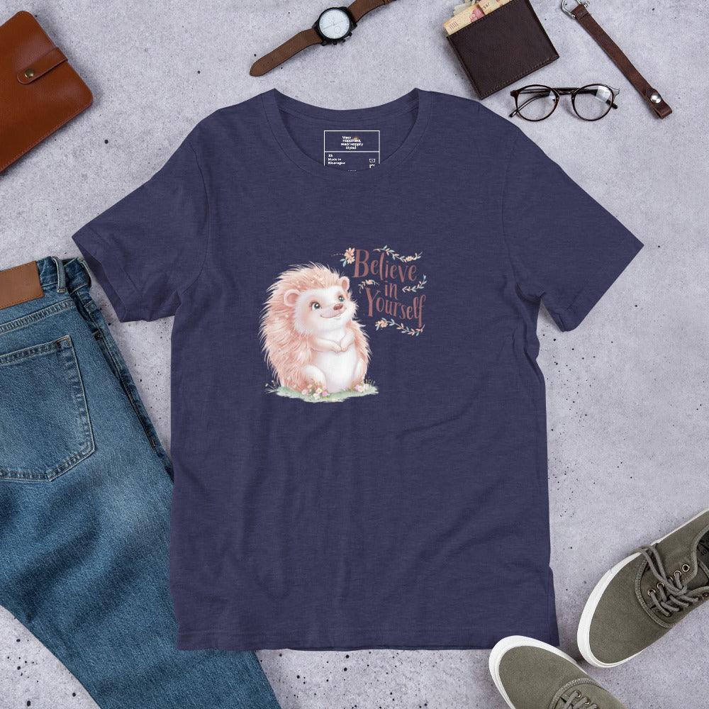 Flat lay of a navy t-shirt with a pastel hedgehog and “Believe in Yourself” quote – cozy motivational tee styled with jeans and accessories.