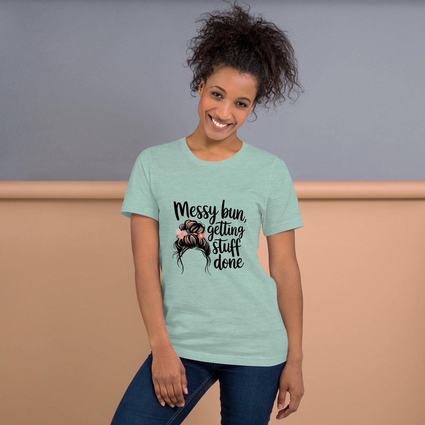 Smiling woman wearing a dusty blue t-shirt with black text that says 'Messy Bun, Getting Stuff Done' and a messy bun illustration