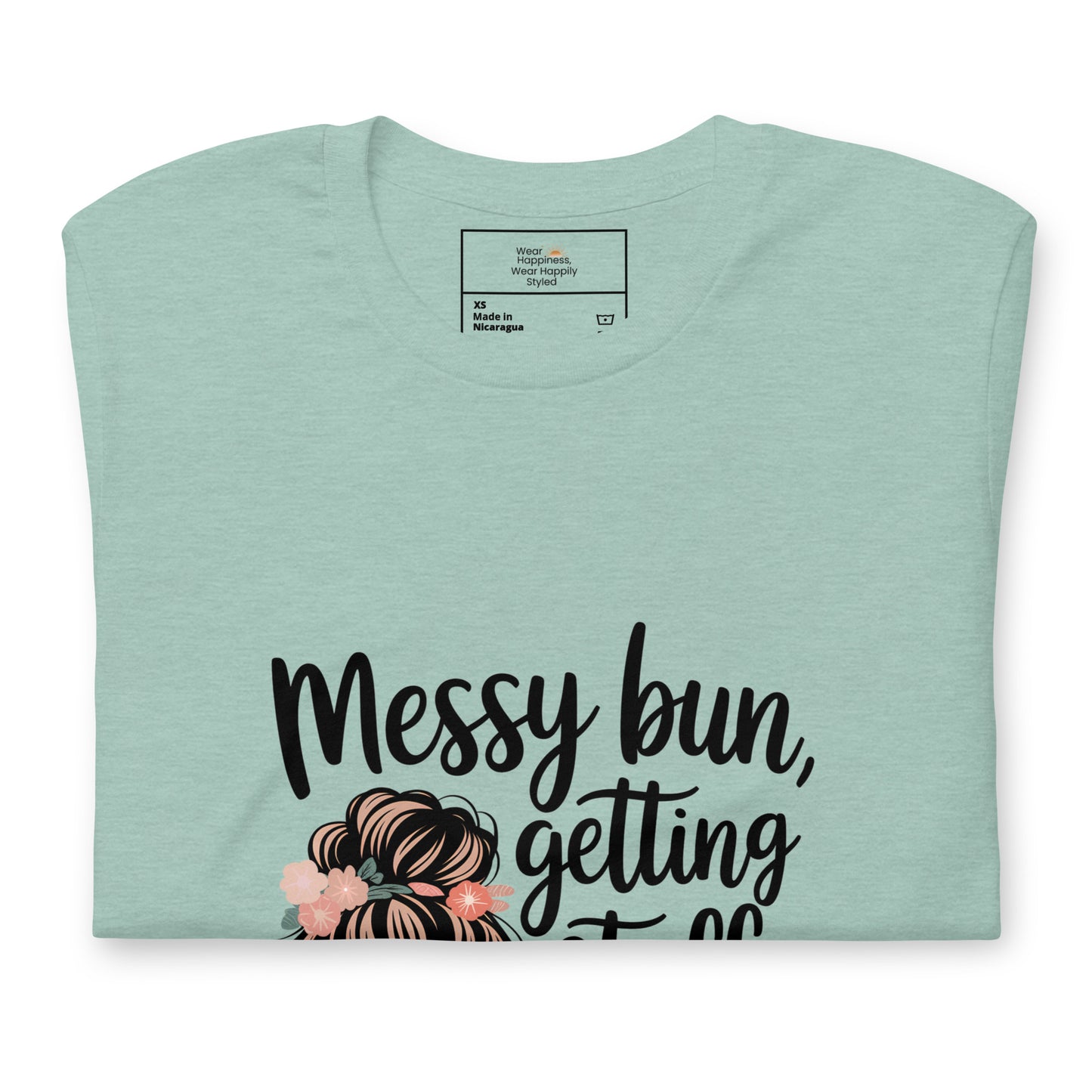 Folded dusty blue t-shirt showing black handwritten text 'Messy bun, getting stuff done' with a messy bun illustration and floral details