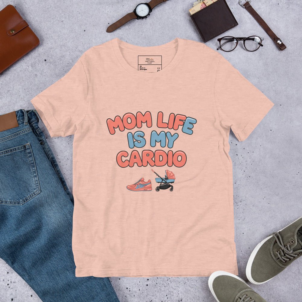 Heather peach unisex t-shirt laid flat on a surface next to jeans and accessories, featuring the phrase 'Mom Life Is My Cardio' in pastel letters with sneakers and pacifier graphic.