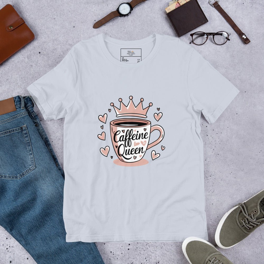 Flat lay of a light blue unisex t-shirt with a pink “Caffeine Queen” coffee cup design, styled with jeans, sneakers, and accessories.