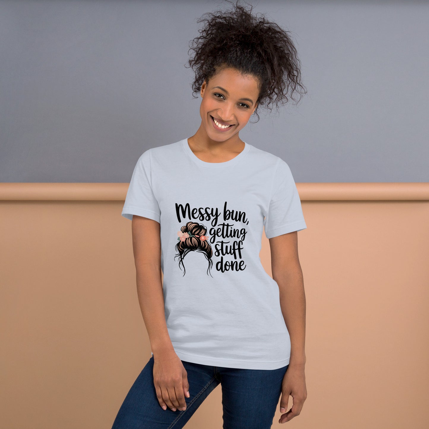 Smiling woman wearing a light blue t-shirt with black text that says 'Messy Bun, Getting Stuff Done' and a messy bun illustration