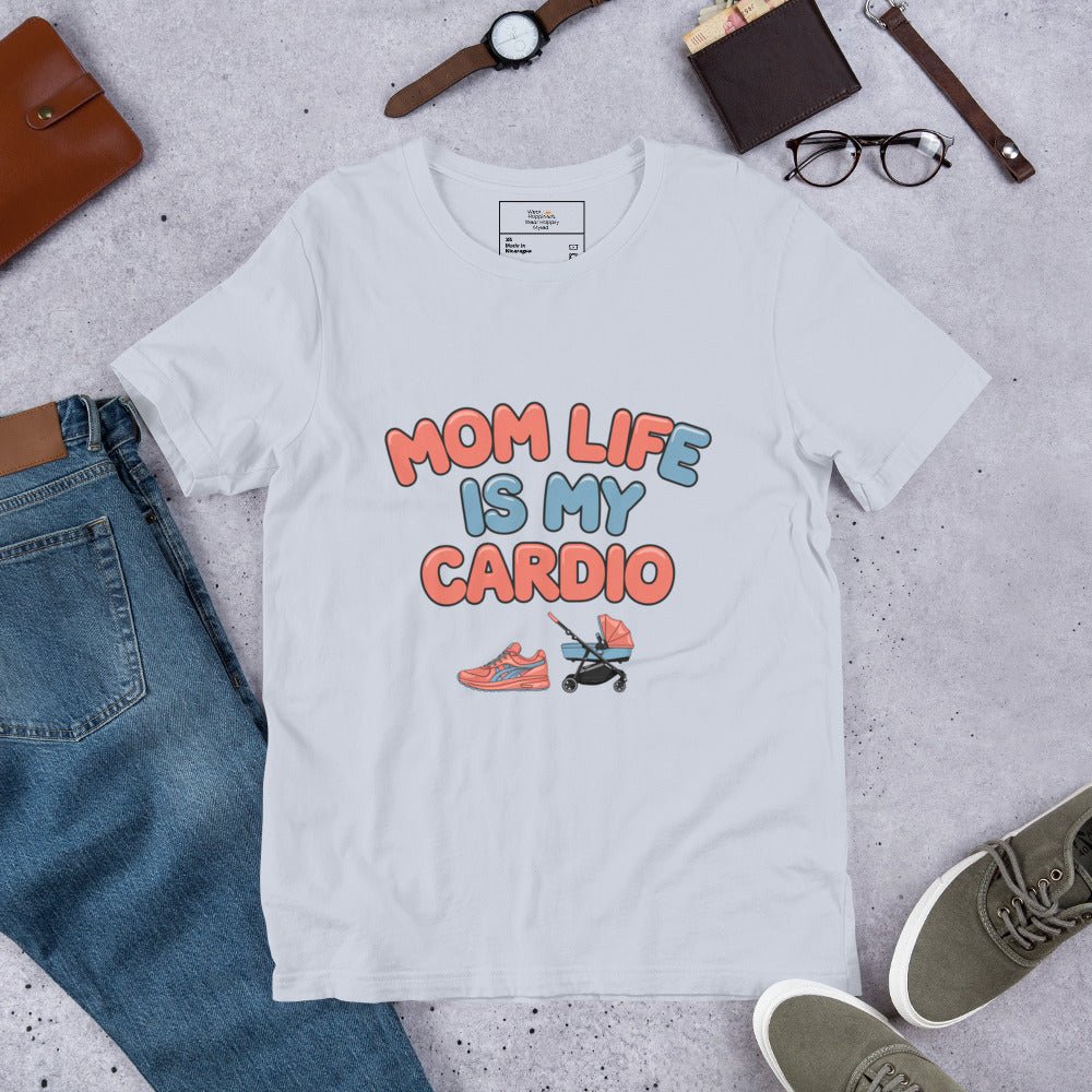 Light blue unisex t-shirt laid flat on a surface next to jeans and accessories, featuring the phrase 'Mom Life Is My Cardio' in pastel letters with sneakers and pacifier graphic.