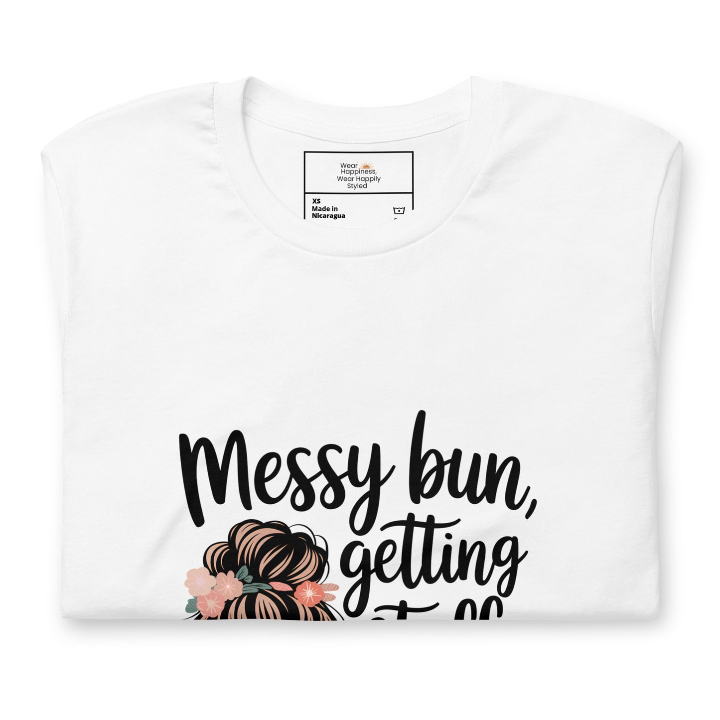 Folded white t-shirt showing black handwritten text 'Messy bun, getting stuff done' with a messy bun illustration and floral details