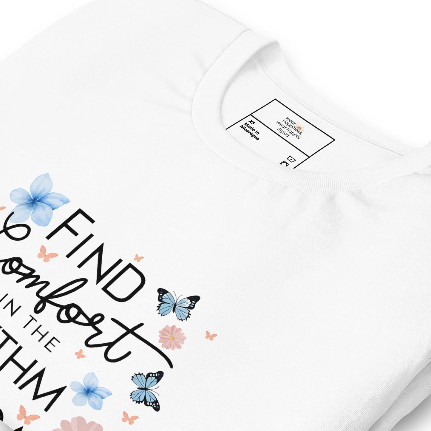 Close-up of a white unisex t-shirt with the inspirational text “Find Comfort in the Rhythm,” decorated with blue butterflies and pastel flowers.