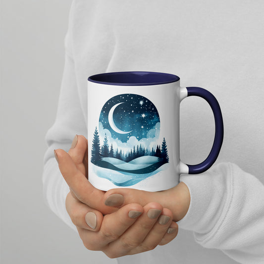 White ceramic mug with dark blue interior, featuring a dreamy moon and forest landscape; held by a person in a white sweater with hands gently wrapped around the mug.