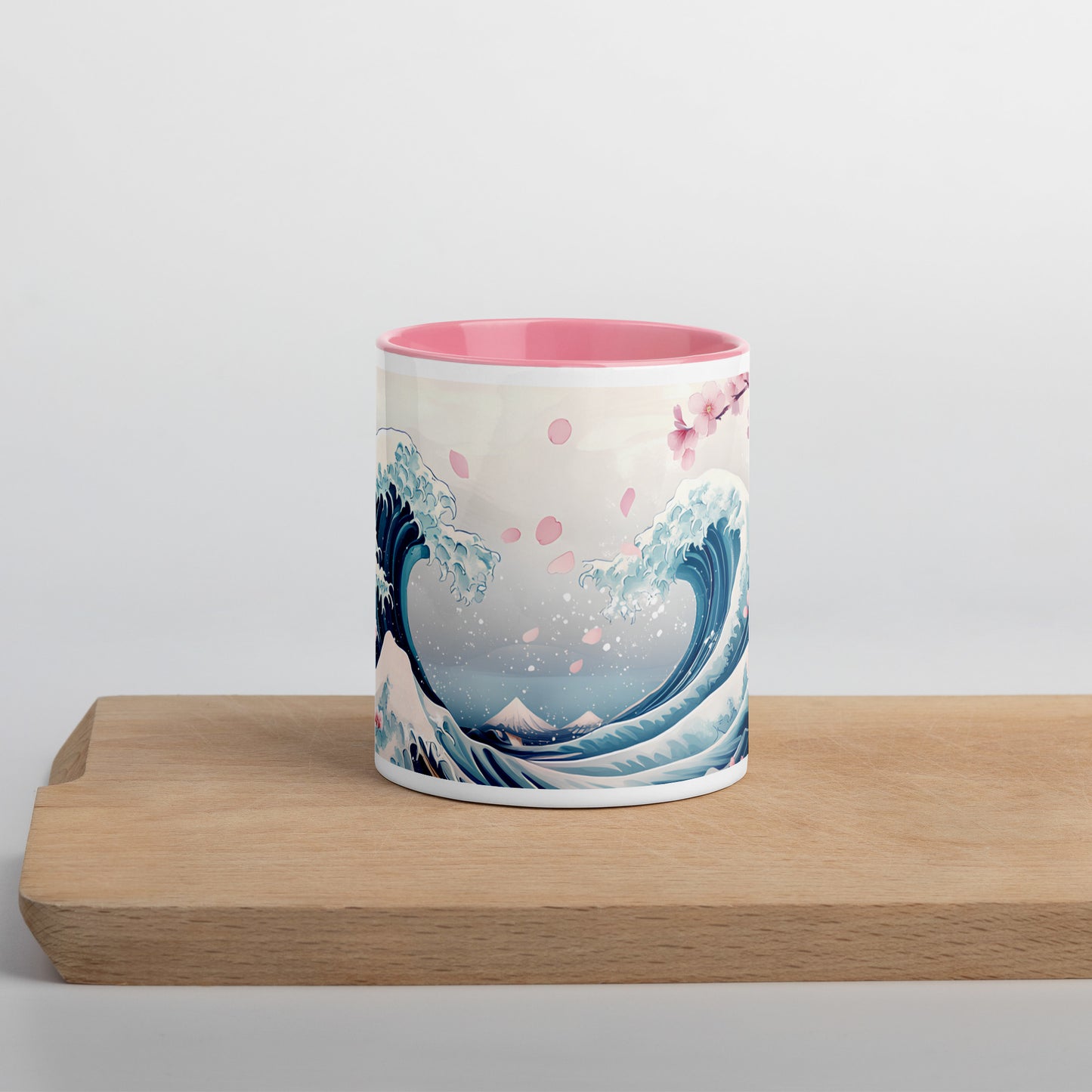 White ceramic mug with pink interior, featuring a cherry blossom and ocean wave design, displayed front-facing on a wooden board with white background.