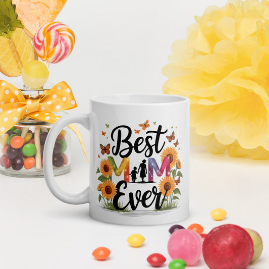 White ceramic mug with floral “Best Mom Ever” design, surrounded by candies and bright yellow decor on a white background.