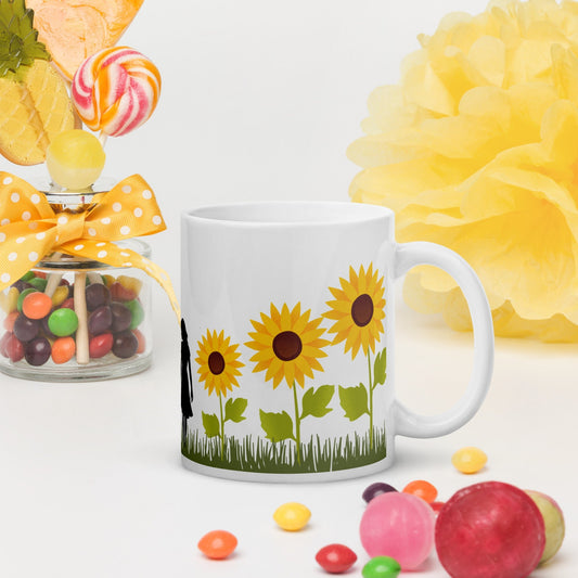 White ceramic mug with sunflower design and handle on the right, placed on a white surface with candy jar and yellow decor in the background.