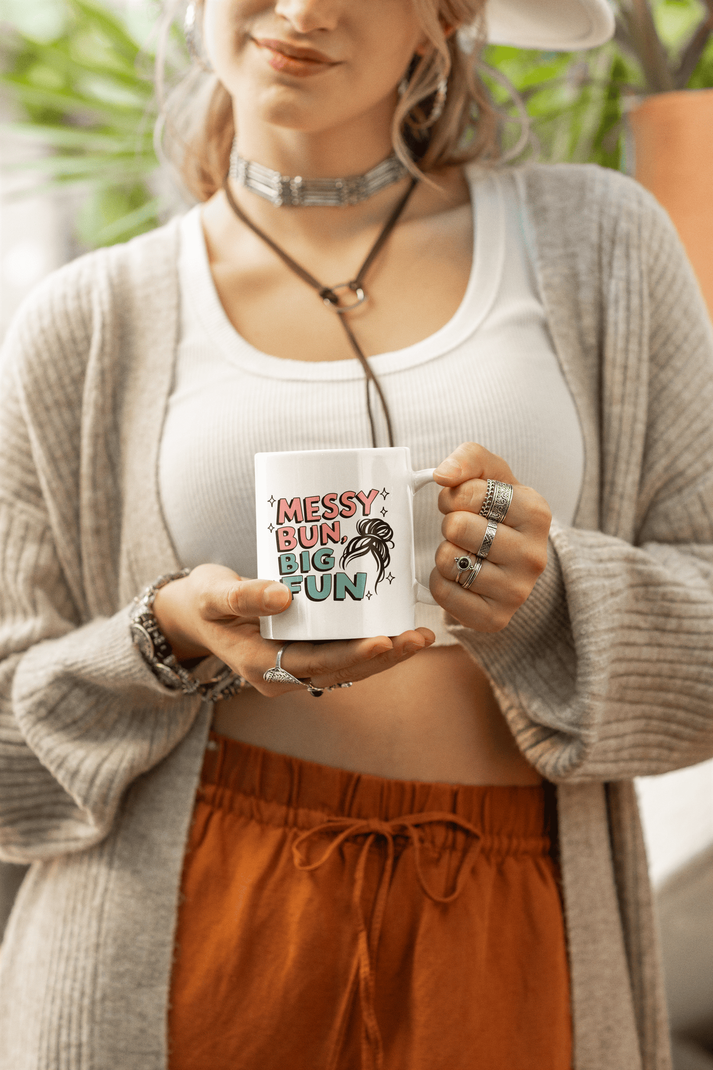 Woman holding white ceramic mug with pastel lettering that says “Messy Bun, Big Fun” and a fun sketch of a messy hairstyle 