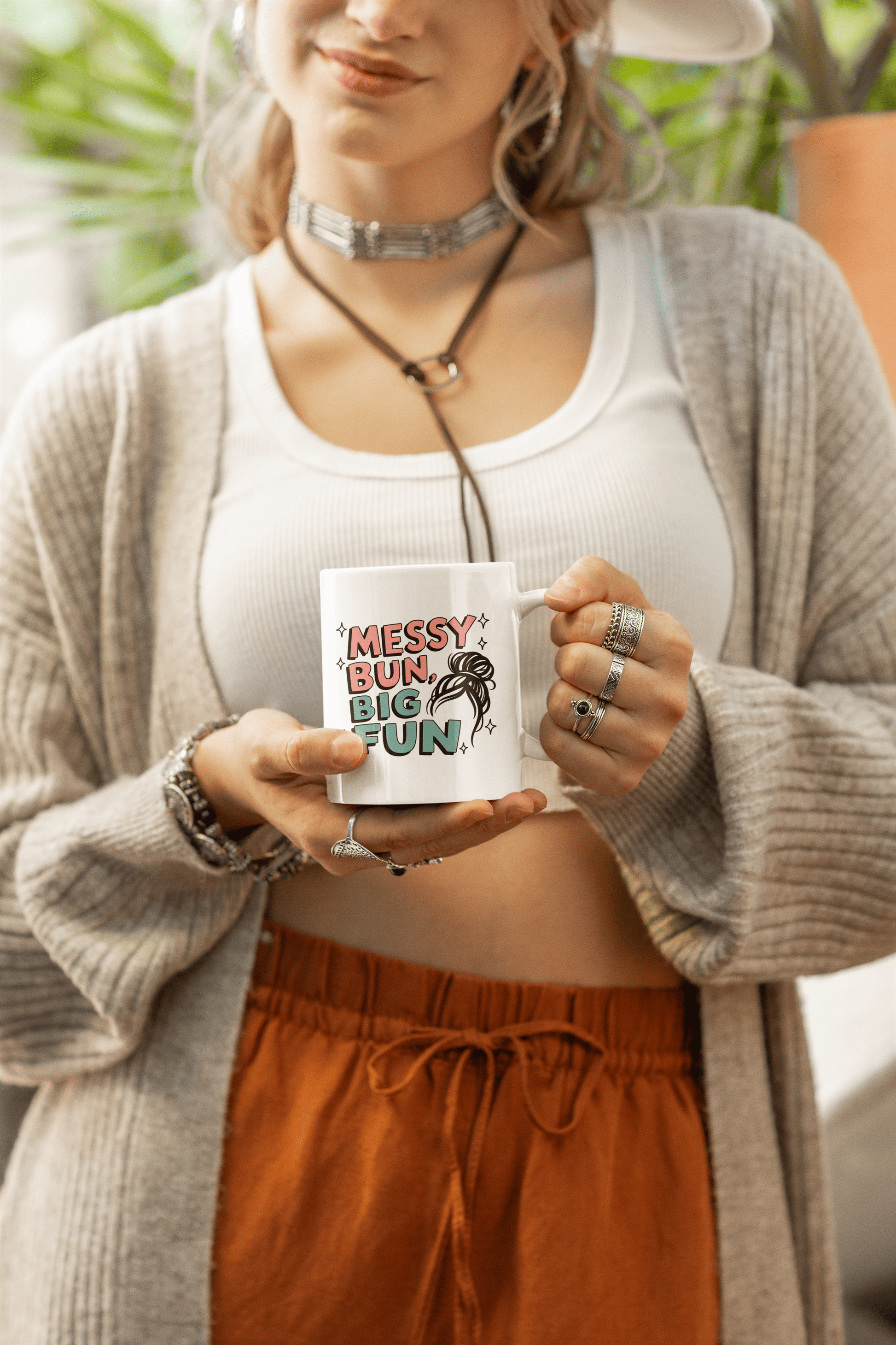 Woman holding white ceramic mug with pastel lettering that says “Messy Bun, Big Fun” and a fun sketch of a messy hairstyle 