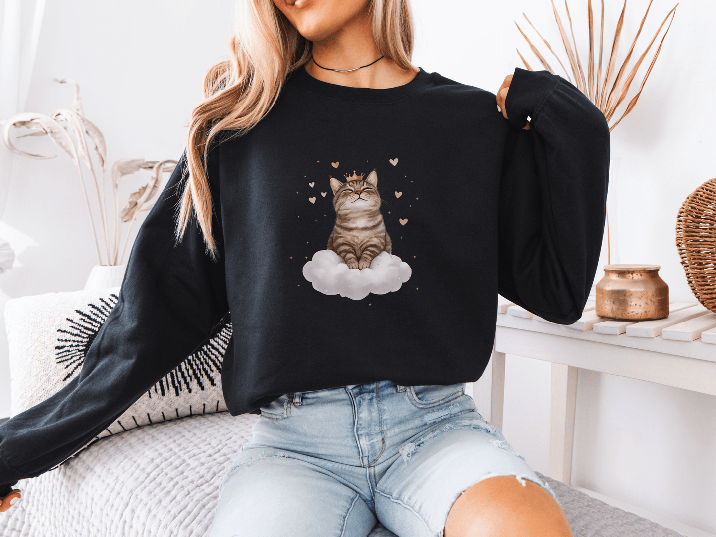 Woman wearing a black sweatshirt featuring a majestic tabby cat sitting on a fluffy cloud, surrounded by soft pink hearts 