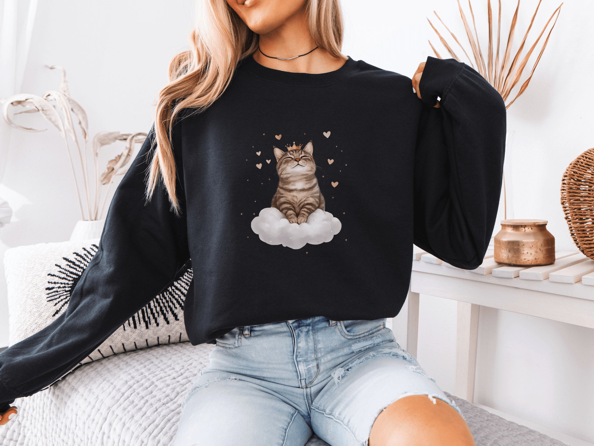 Woman wearing a black sweatshirt featuring a majestic tabby cat sitting on a fluffy cloud, surrounded by soft pink hearts 