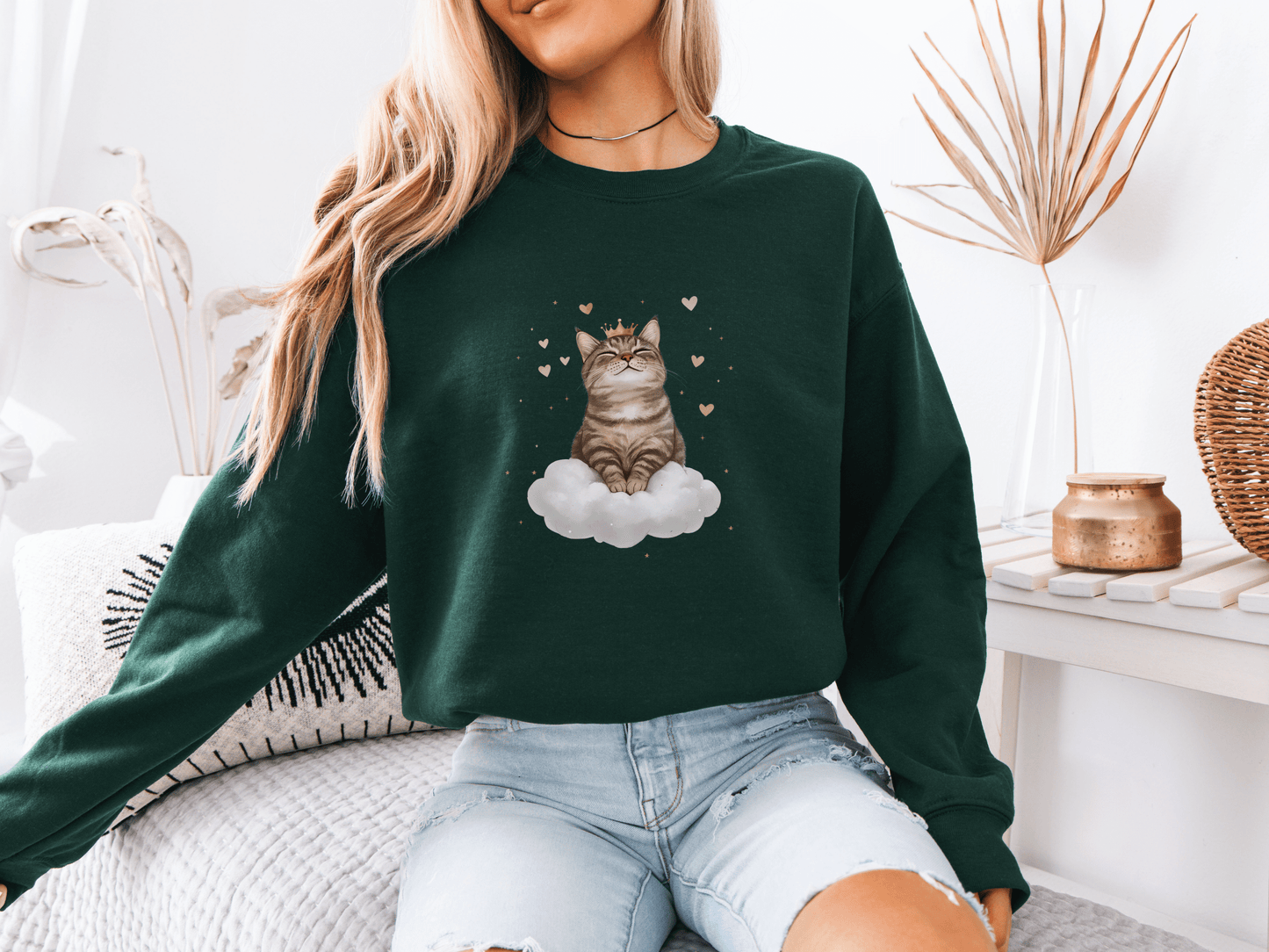 Woman wearing a forest green sweatshirt featuring a majestic tabby cat sitting on a fluffy cloud, surrounded by soft pink hearts 