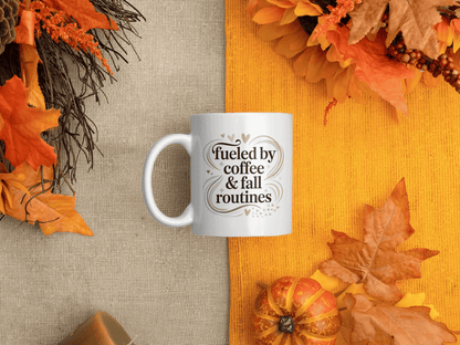 White mug with “Fueled by coffee & fall routines” quote, styled on a cozy autumn background with orange leaves, pumpkins, and warm rustic tones.