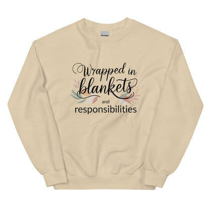 Beige sweatshirt with text 'Wrapped in blankets and responsibilities' on a white background