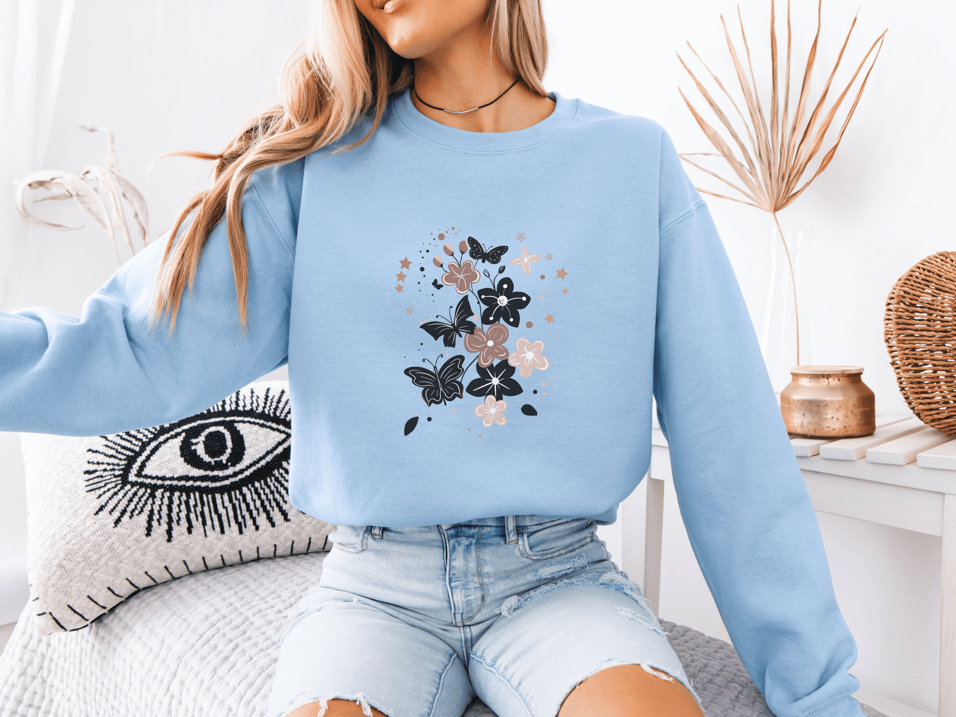 Woman wearing a light blue sweatshirt featuring elegant black and blush butterflies and flowers – a soft and stylish gift for moms who love whimsical bloom designs.