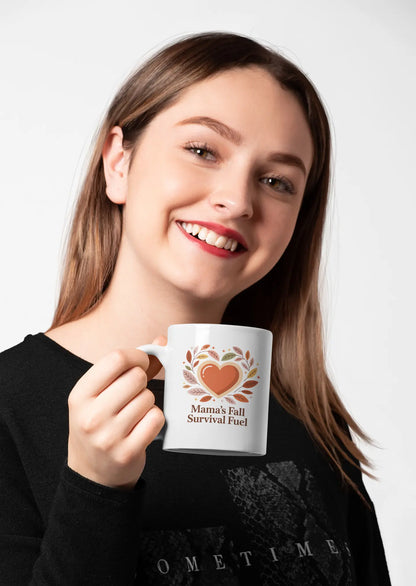 Woman holding a mug with a heart design and text "Mama's Fall Survival Fuel" on a white background